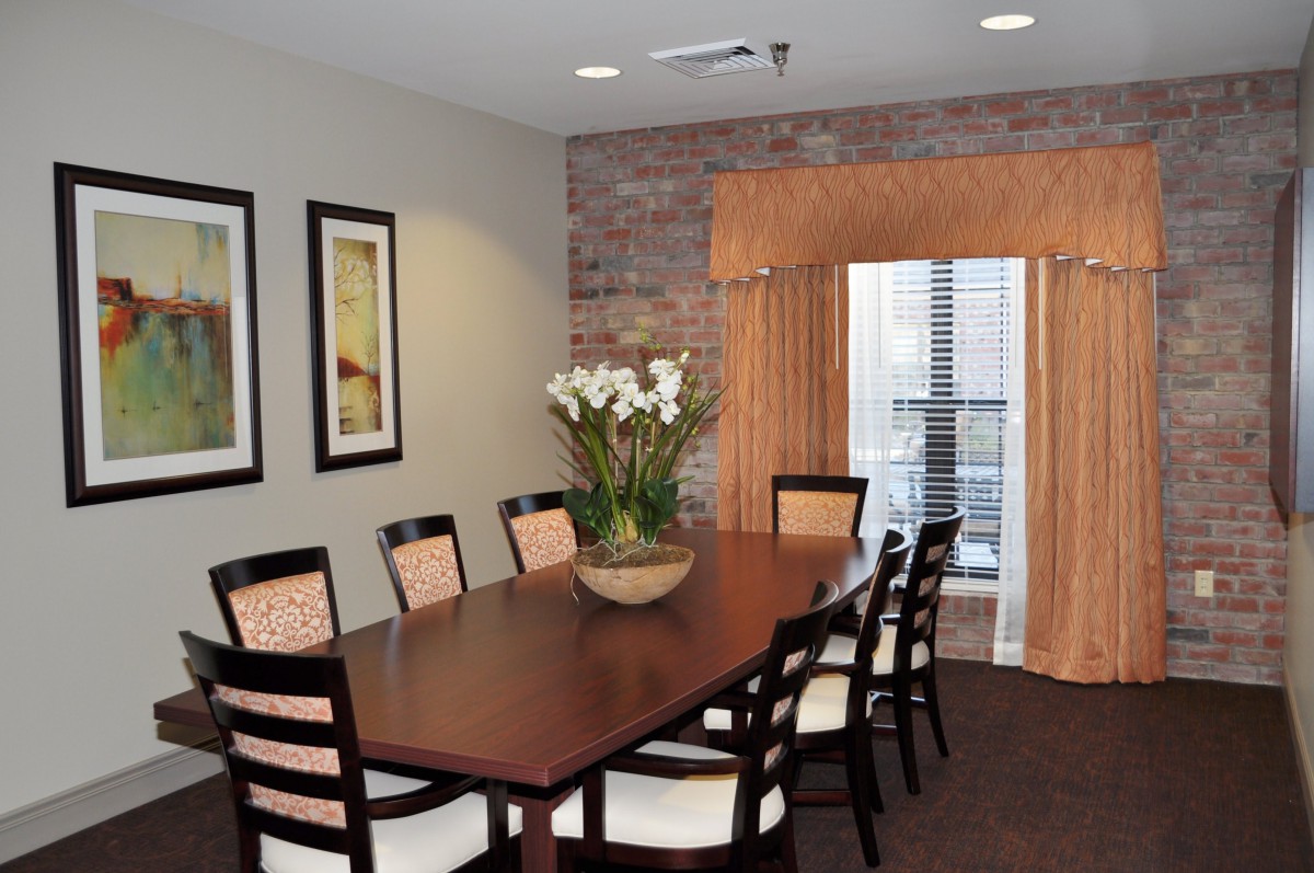 A stylish dining room with a long wooden table, cushioned chairs, and decorative elements including framed wall art and a flower arrangement.