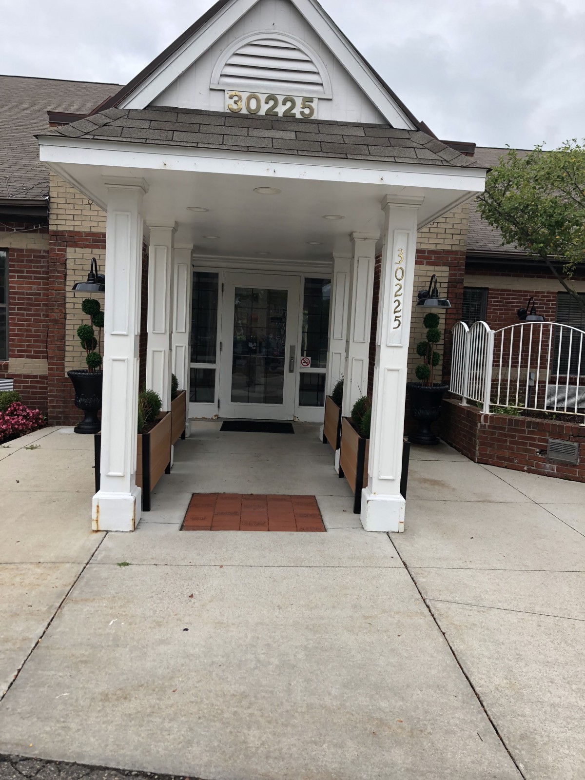 The entrance to a brick building with white columns and potted plants.