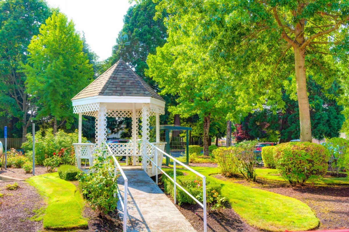 A picturesque garden with a white gazebo surrounded by lush greenery and trees.