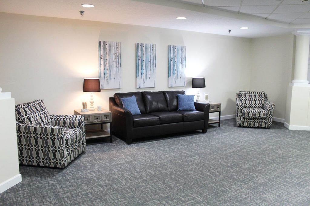 A well-furnished living room with a black sofa, patterned armchairs, and artwork on the wall.