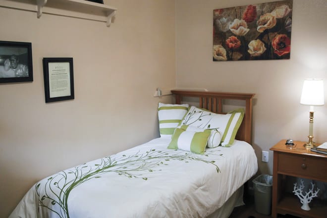 A cozy bedroom with a single bed adorned with green and white bedding, featuring floral artwork on the wall.