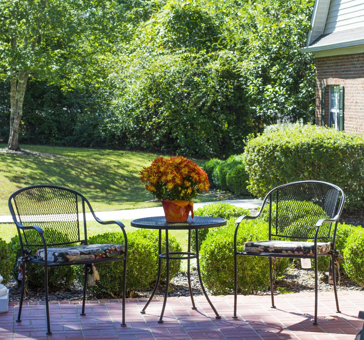 A peaceful patio setting with two chairs and a table adorned with flowers, overlooking a lush garden.