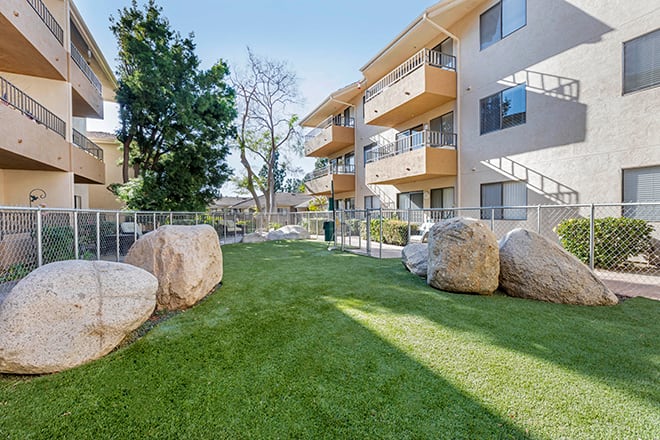 A residential apartment complex featuring a well-maintained lawn and large decorative rocks in the outdoor area.