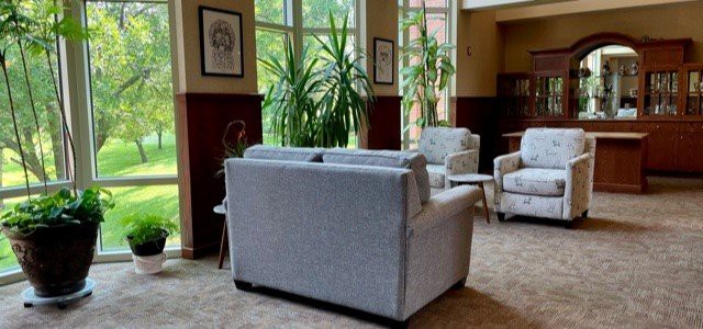 A cozy lobby area with sofas, chairs, and greenery by large windows.
