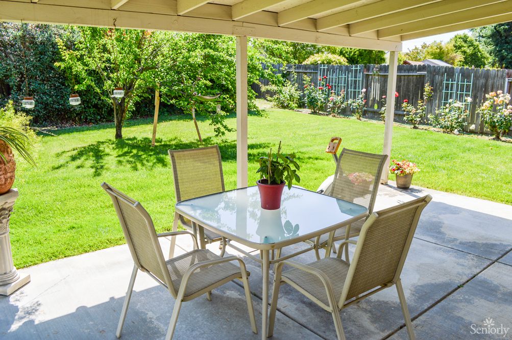 A cozy patio setup with a glass table and four chairs overlooking a lush green backyard.