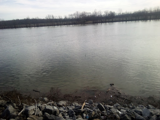 A serene view of a river bordered by rocky terrain under a cloudy sky.