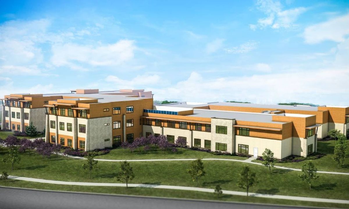 A modern school building with expansive glass windows and a green landscape under a clear blue sky.