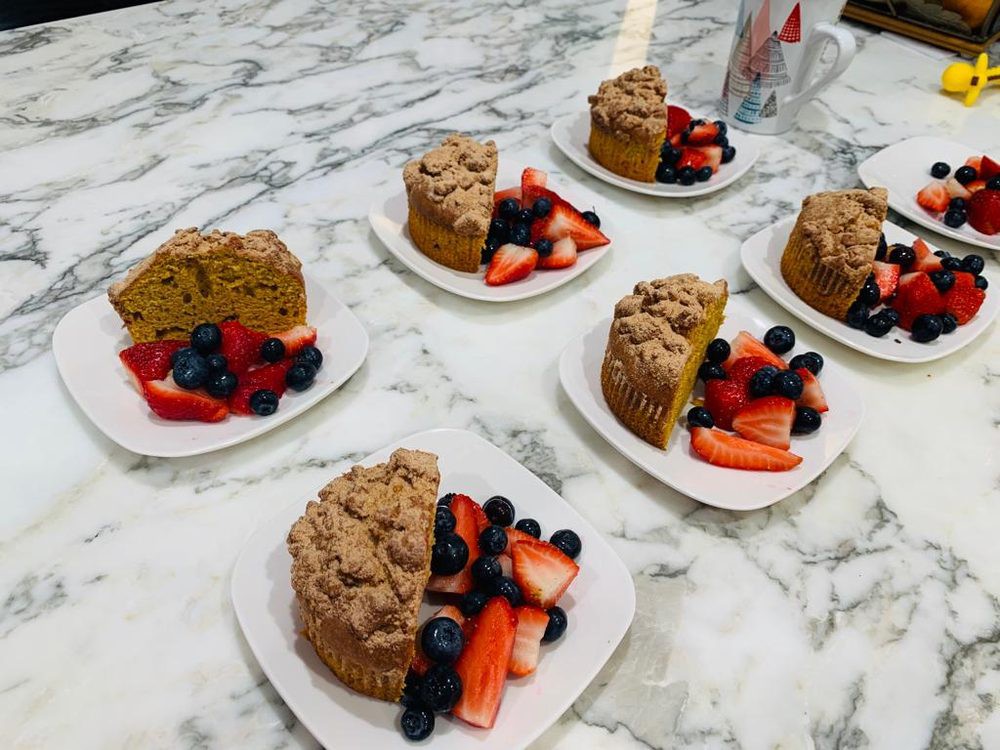 Slices of crumb cake served with fresh strawberries and blueberries on a marble table.
