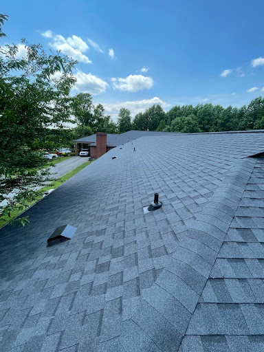 A panoramic view of a residential roof with shingles, showcasing clear blue skies and surrounding greenery.