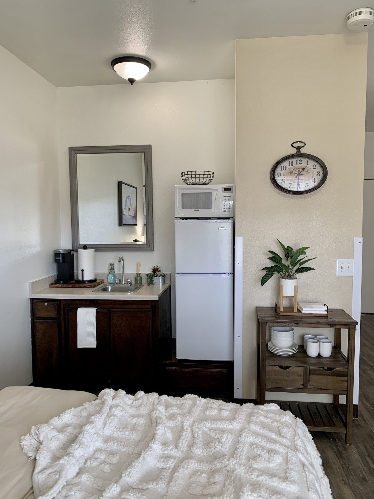 A cozy bedroom nook featuring a small fridge, coffee station, and minimalist decor.