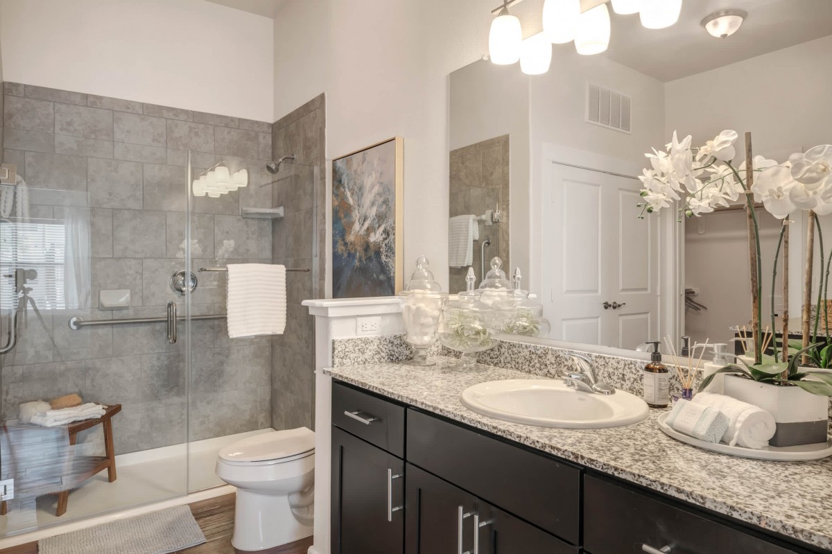 A modern bathroom featuring a granite countertop, glass-enclosed shower, and elegant lighting.