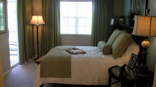A cozy bedroom with a bed, green curtains, and a floor lamp.
