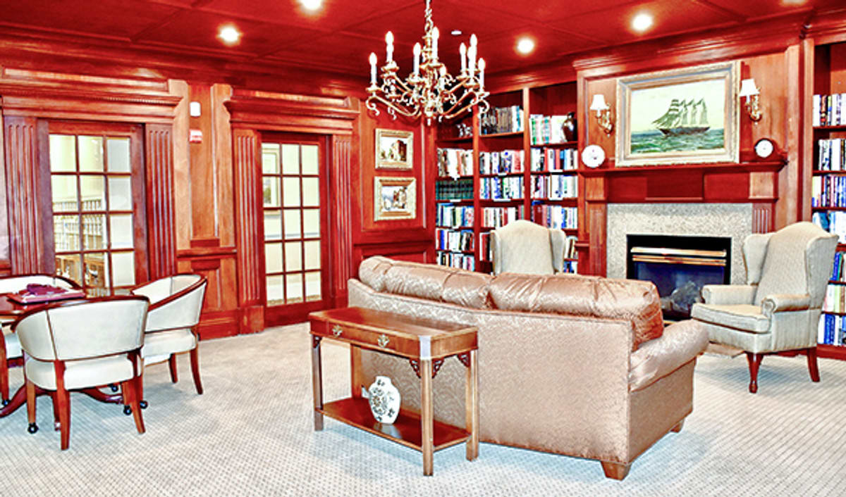 A luxurious living room with a cozy library corner, featuring wood paneling, a leather sofa, and a chandelier.