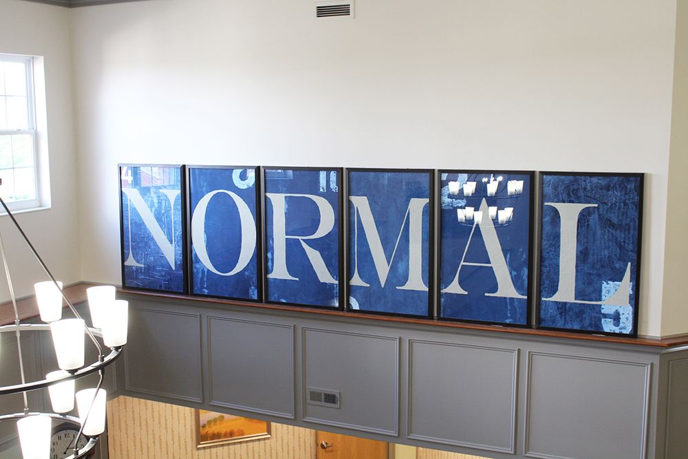 A modern art installation featuring the word 'NORMAL' displayed across multiple panels with a blue background.