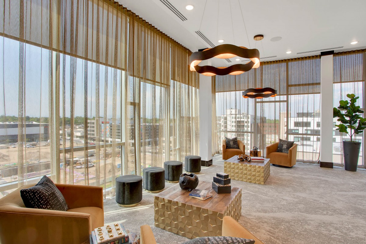 A modern lounge with large windows offering a city view, featuring contemporary seating and decor.
