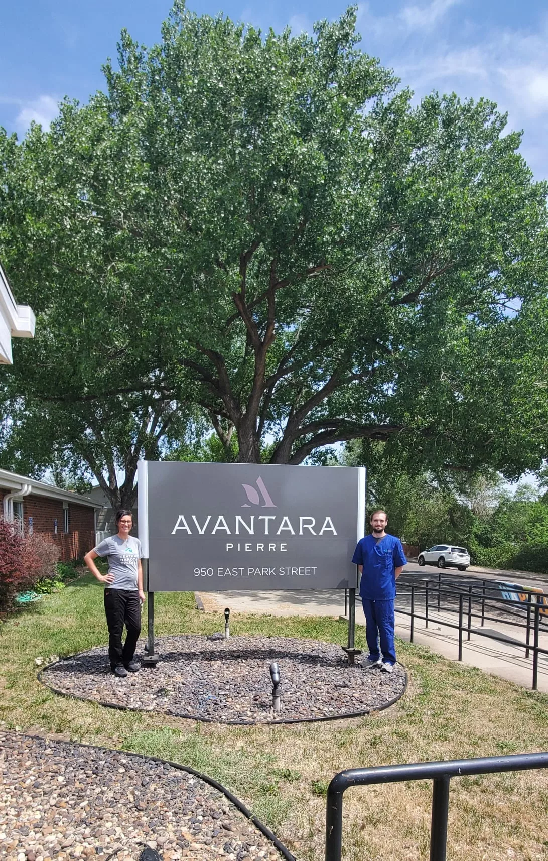 Two individuals stand beside the Avantara Park Ridge sign outdoors.