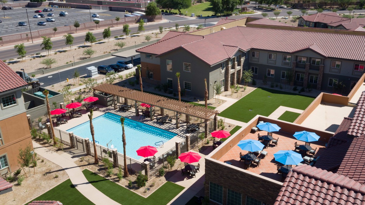 Aerial view of a residential complex featuring a swimming pool, outdoor seating with colorful umbrellas, and landscaped areas.
