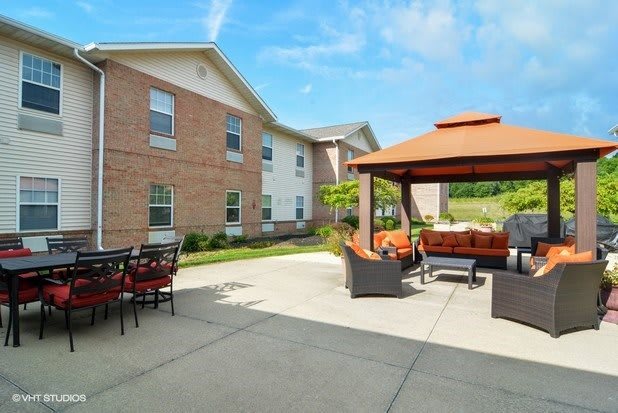 A cozy outdoor patio area with comfortable seating under a gazebo, adjacent to a brick building on a sunny day.