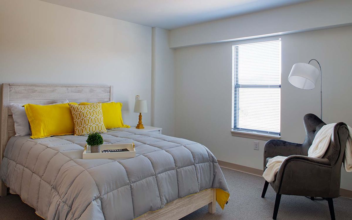A minimalist bedroom with a cozy bed featuring yellow accents and a large window.
