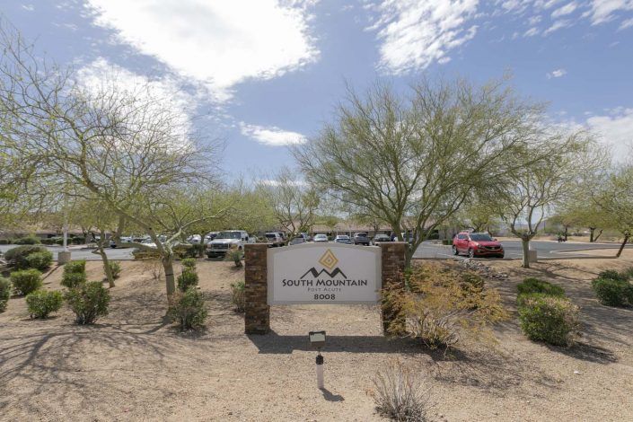 A desert landscape with a sign and parking lot on a cloudy day.
