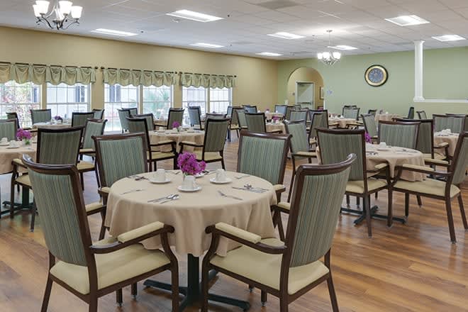 A neatly arranged dining room with round tables and upholstered chairs.