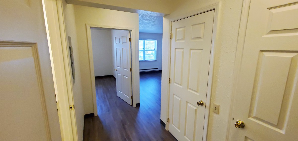 A hallway with two doorways leading to rooms in an apartment, featuring wooden floors and light-colored walls.
