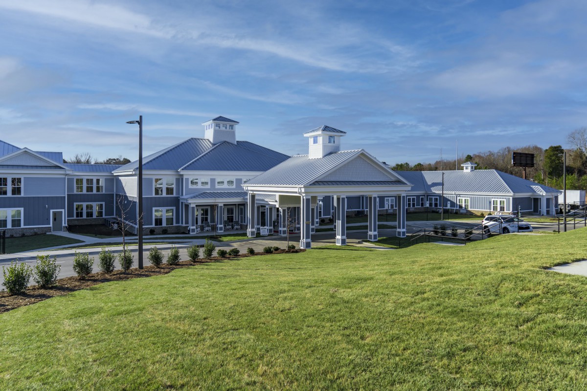 A large building with a white exterior and a spacious front lawn under a clear blue sky.