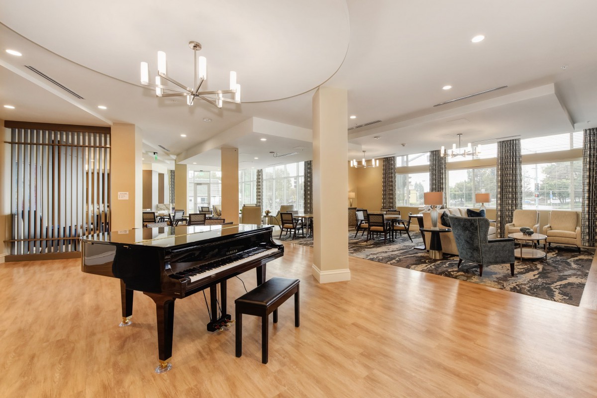 A modern and spacious interior featuring a grand piano, hardwood floors, and a dining area with large windows.