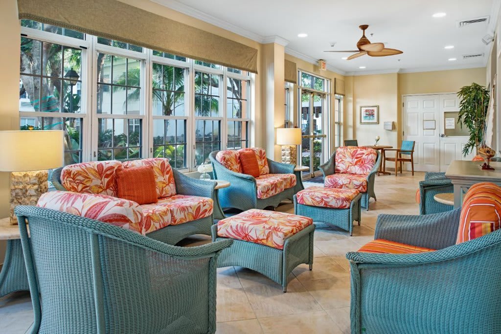 A cozy living room with wicker furniture and floral cushions, flooded with natural light from large windows.