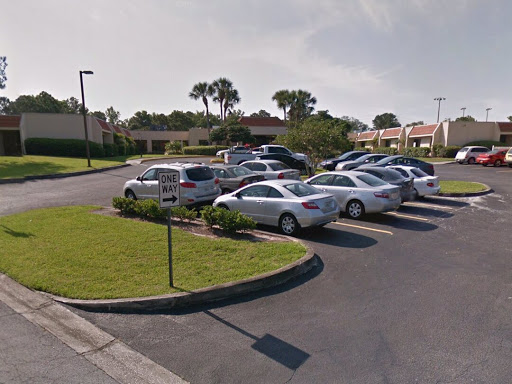A view of a parking lot filled with various cars surrounded by green grass.