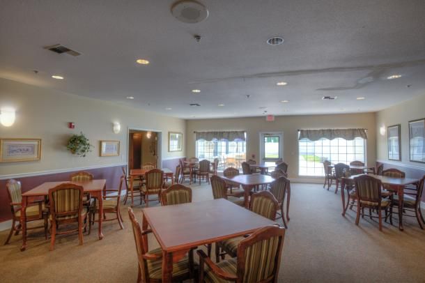 An empty dining room with several tables and chairs, well-lit by natural light through the windows.