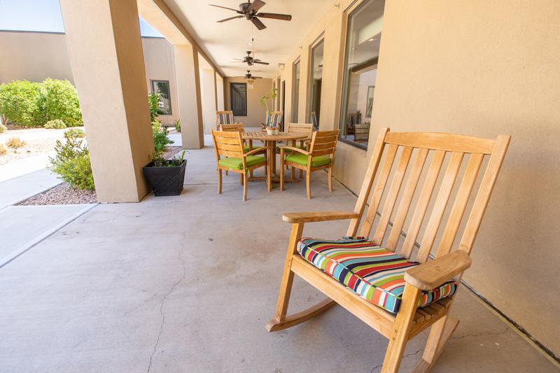 A cozy outdoor patio area featuring a wooden rocking chair with colorful cushions, a dining set, and ceiling fans for comfort.