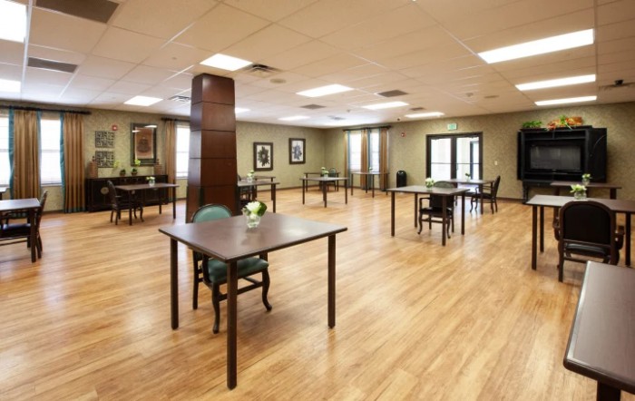 A spacious room with wooden flooring, featuring tables and chairs arranged for an event or gathering.