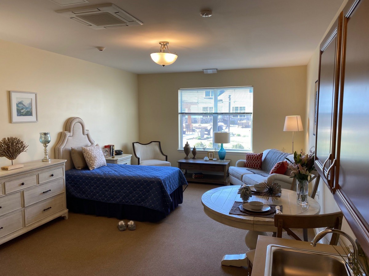 A cozy bedroom featuring a bed, sofa, table, and window with ample natural light.