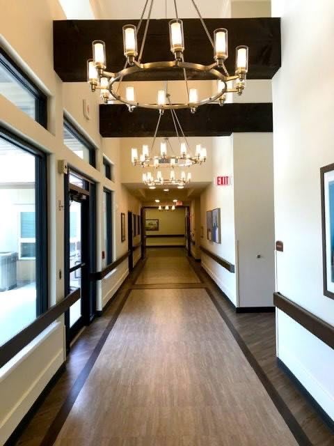 A well-lit hallway with chandeliers and windows along the side.