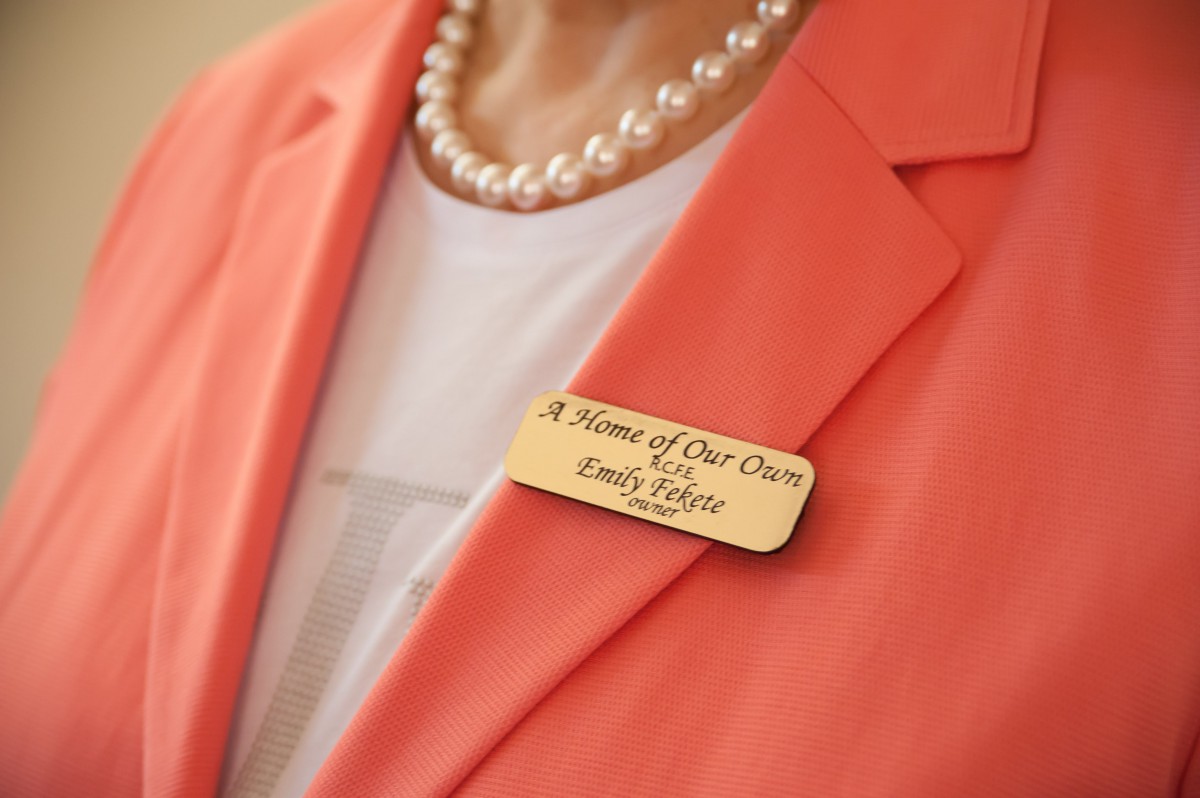 A person wearing a name tag, a pearl necklace, and an orange blazer.