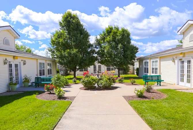 A sunny residential courtyard with a pathway, surrounded by trees and landscaped greenery.