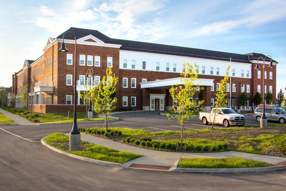 A modern hospital building with a neatly landscaped exterior and a parking area in the foreground.