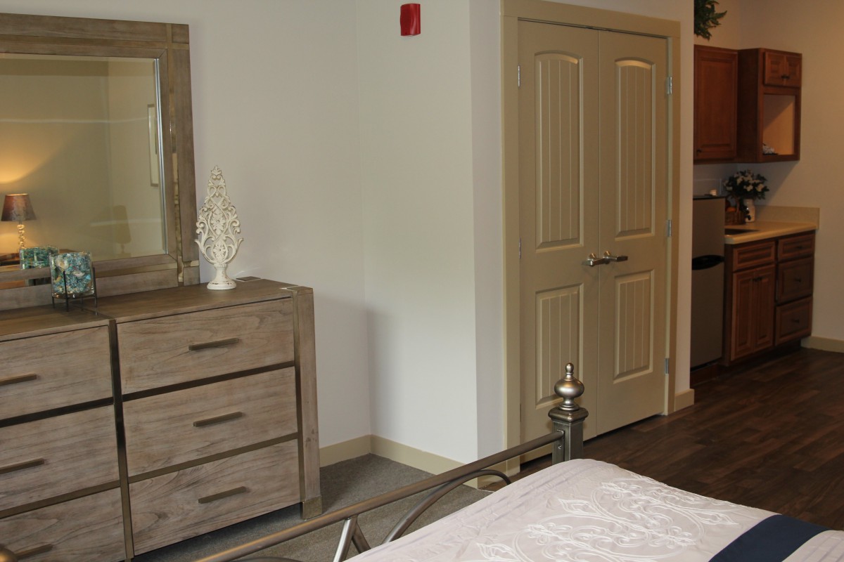 A cozy bedroom featuring a wooden dresser with a mirror and a partially visible bed.