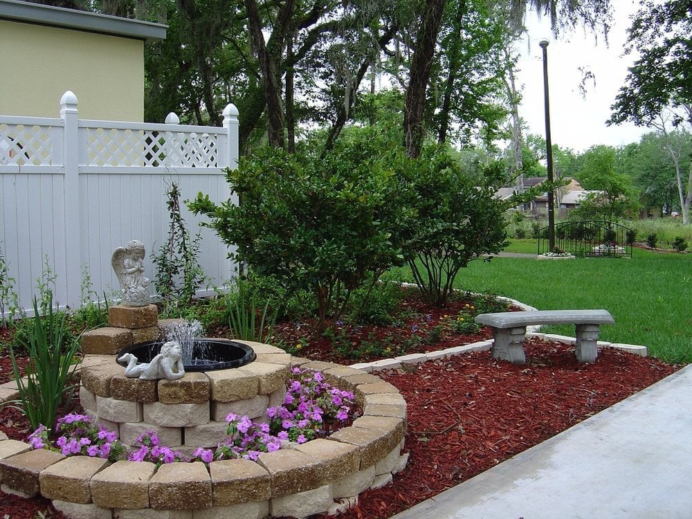 A beautifully landscaped garden with a small water fountain, vibrant flowers, and a stone bench.