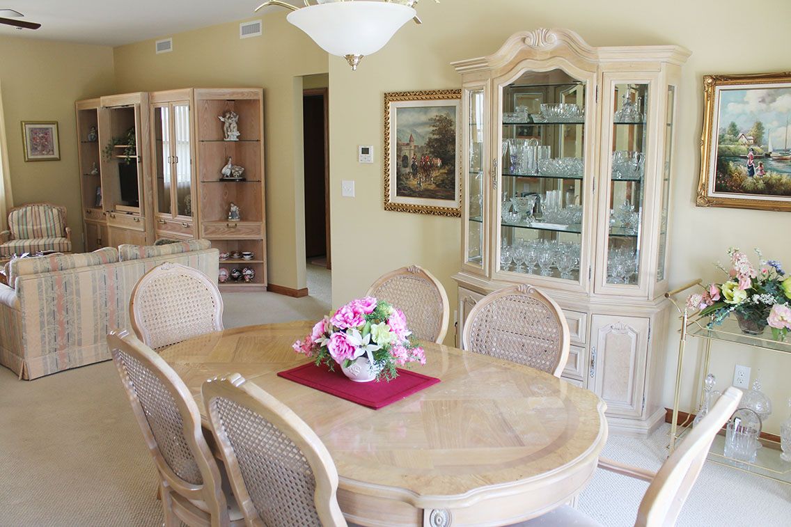 A cozy dining room featuring an elegant table with a floral centerpiece, surrounded by chairs and a china cabinet displaying fine glassware.