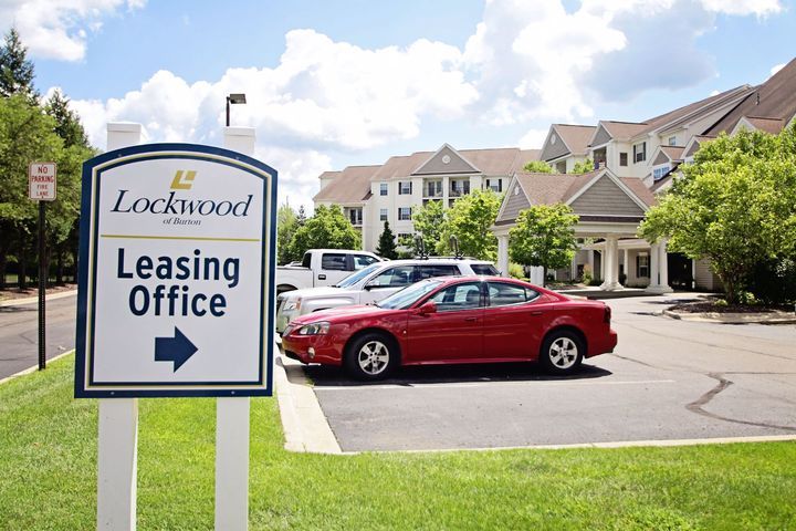 A view of a leasing office sign in front of an apartment complex with cars parked nearby.