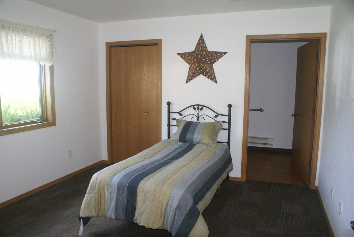 A simple bedroom featuring a single bed with striped bedding and a large star decoration on the wall.