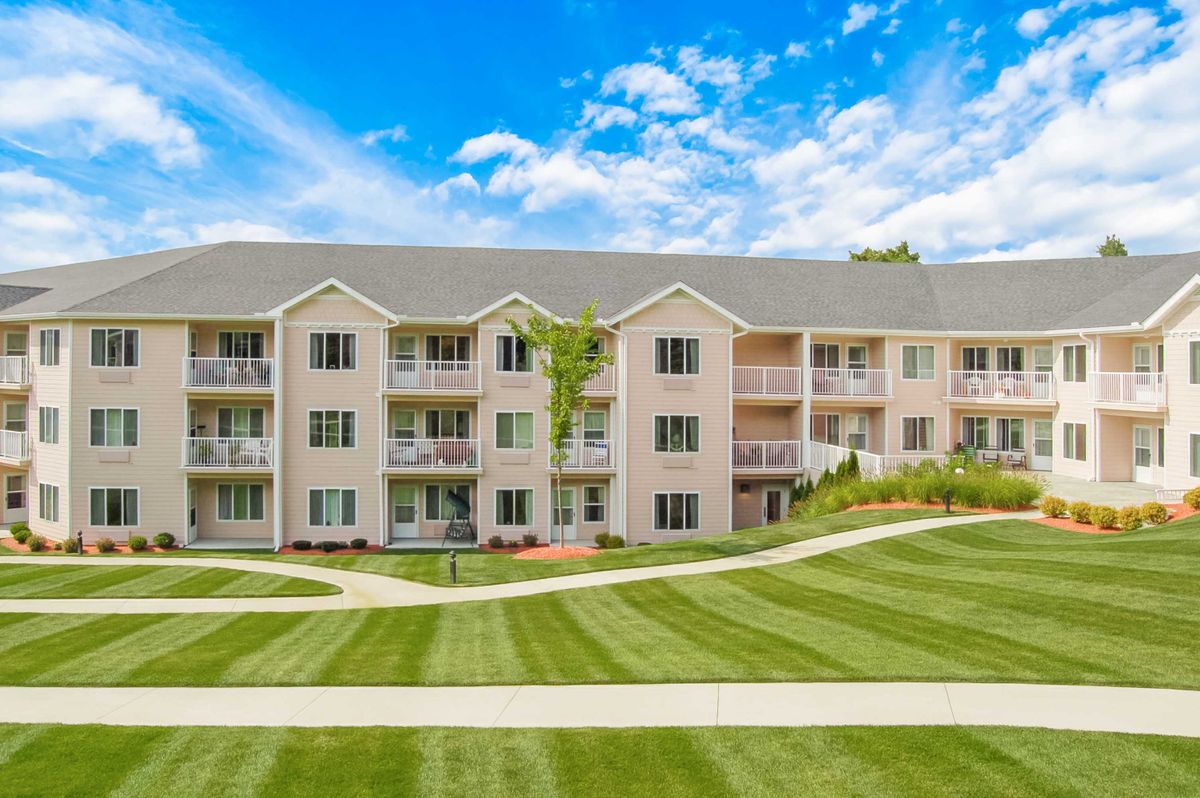 A three-story residential apartment building with well-maintained lawns and clear blue skies.