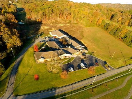 Aerial view of a building surrounded by autumn trees and a road with parked cars.