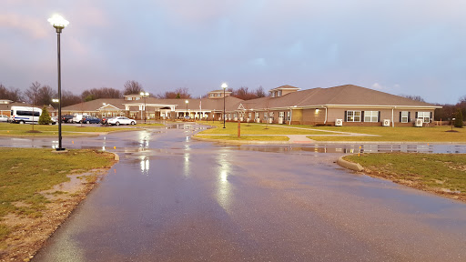 A view of a medical facility during a rainy evening, reflecting lights on the wet pavement.