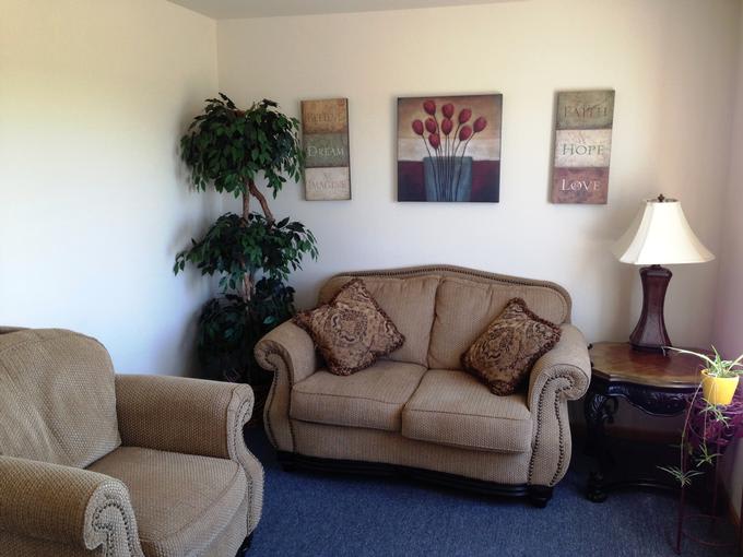 A cozy living room with a sofa, armchair, indoor plant, and wall art.