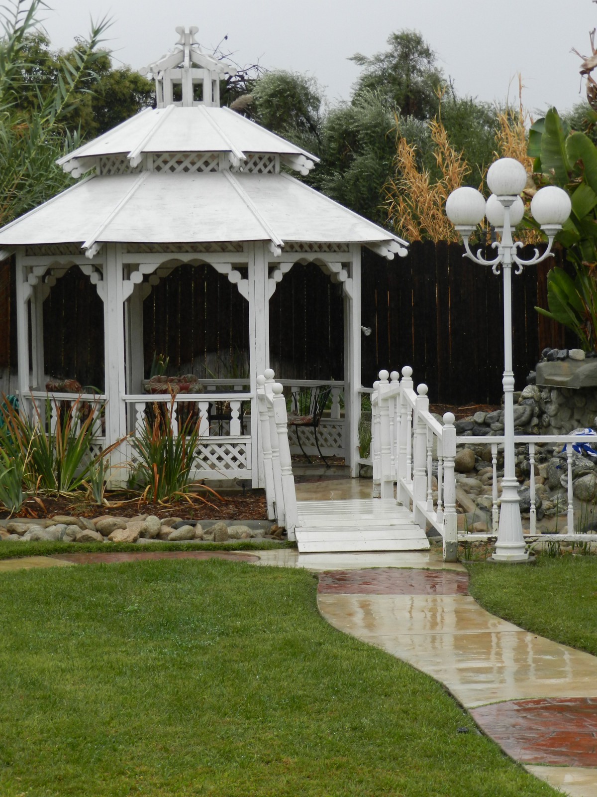 A white gazebo in a landscaped garden with a pathway and a lamp post.