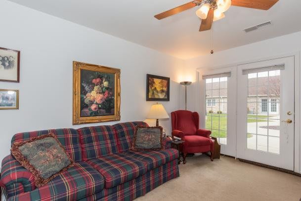 A cozy living room featuring a plaid sofa, red armchair, ceiling fan, and decorative artwork.