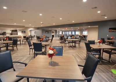 An empty dining room with neatly arranged tables and chairs, featuring a floral centerpiece on each table.